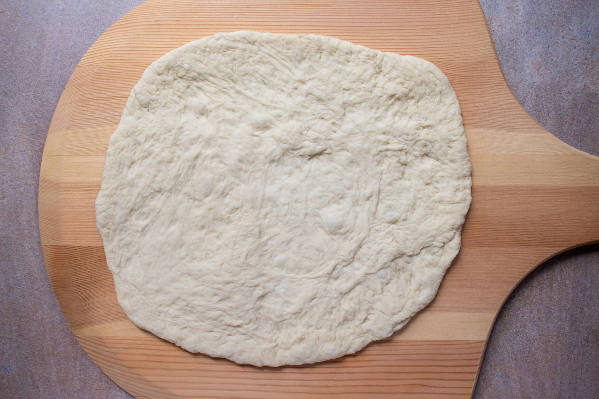 Pizza dough stretched out on a wooden pizza peel.