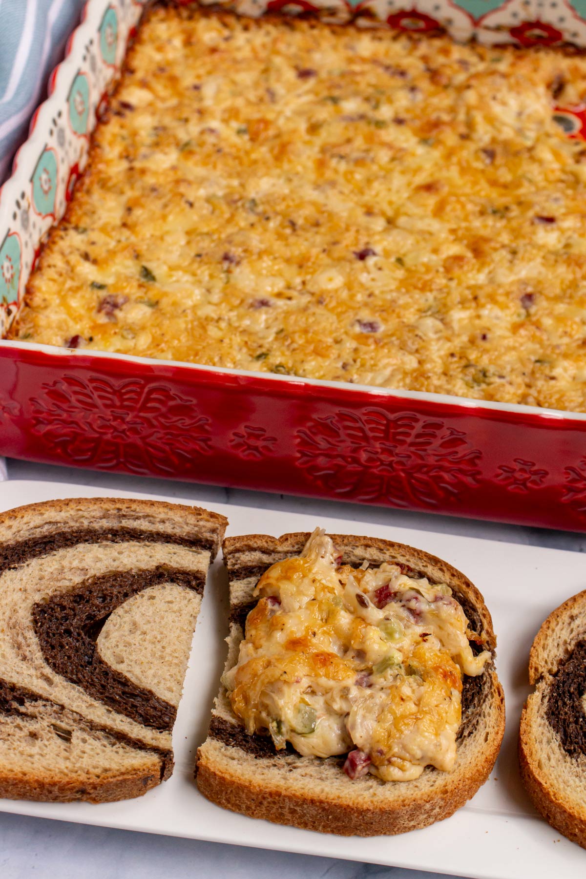 Rye bread slices topped with Reuben dip with a colorful baking dish of dip behind them.