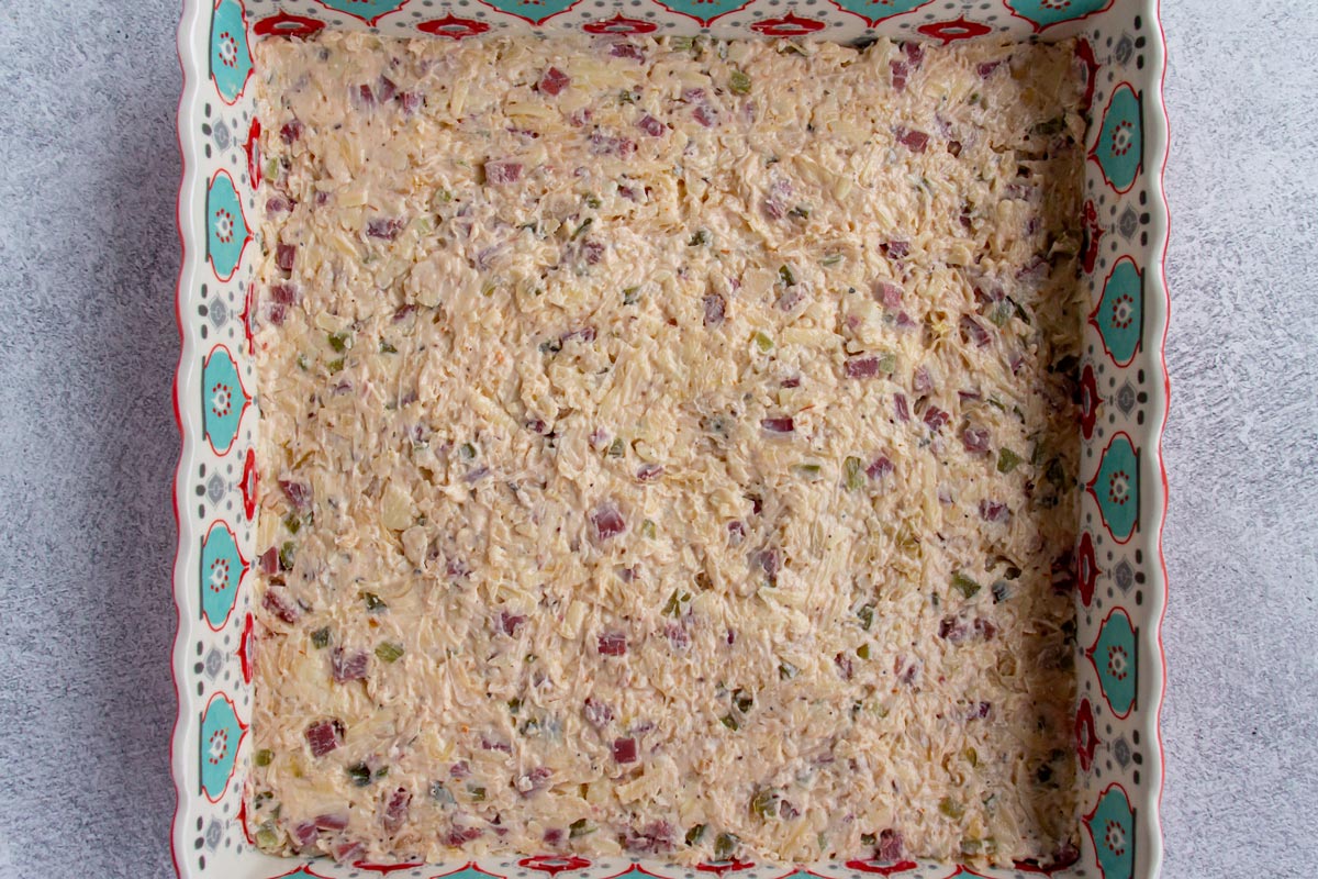 Unbaked Reuben dip in a colorful square baking dish on a light grey background.