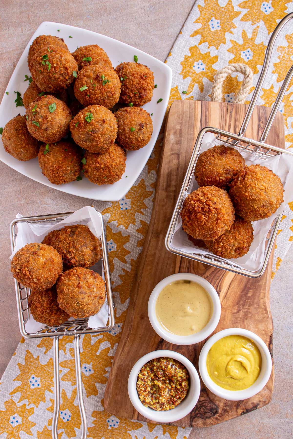 Bitterballen served on a white plate and small metal baskets with small cups of mustard.