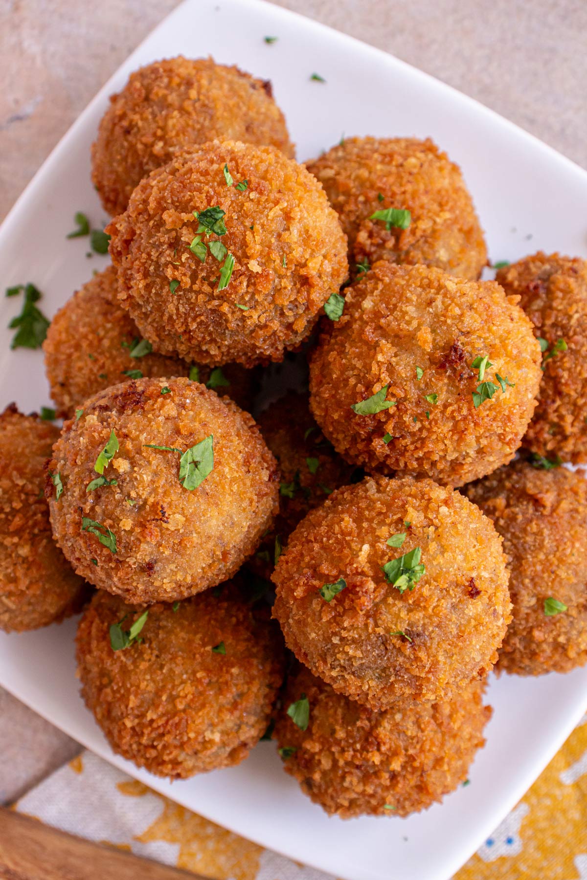 Closeup of fried bitterballen topped with chopped parsley piled high on a white plate.