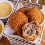 Closeup of a basket of bitterballen with one bitten into showing the interior.