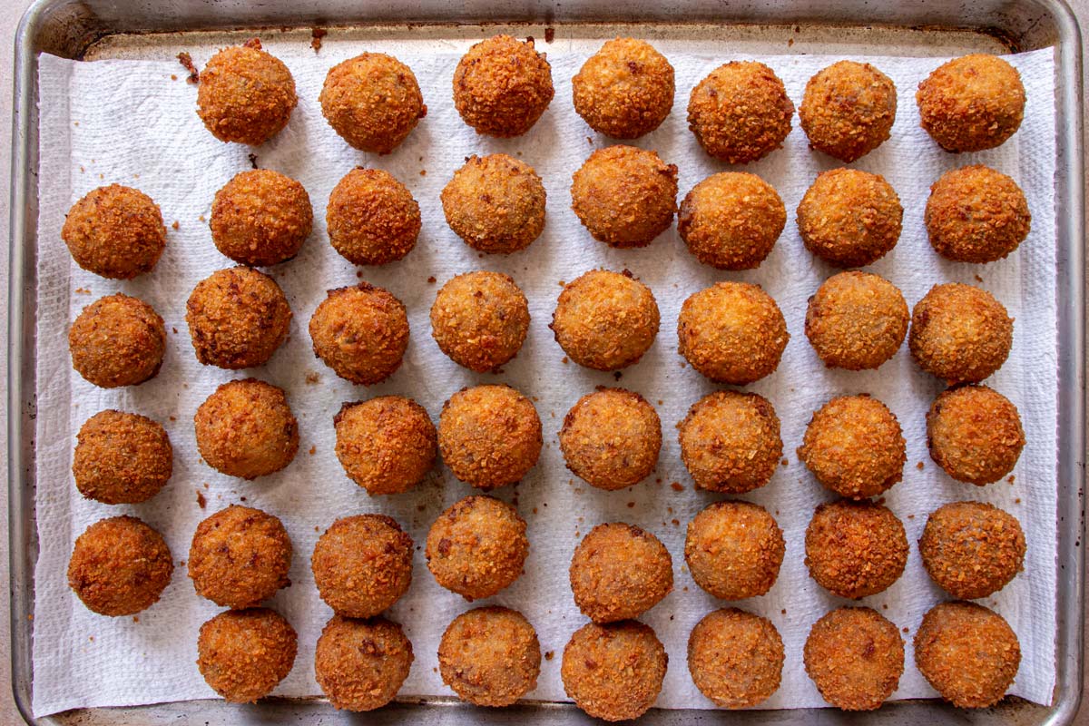 Breaded fried balls on a paper towel lined baking sheet.