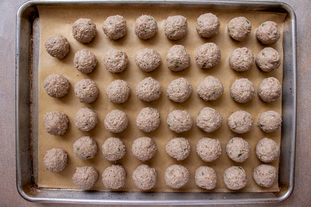 Meatballs arranged in rows on a parchment paper lined baking sheet.