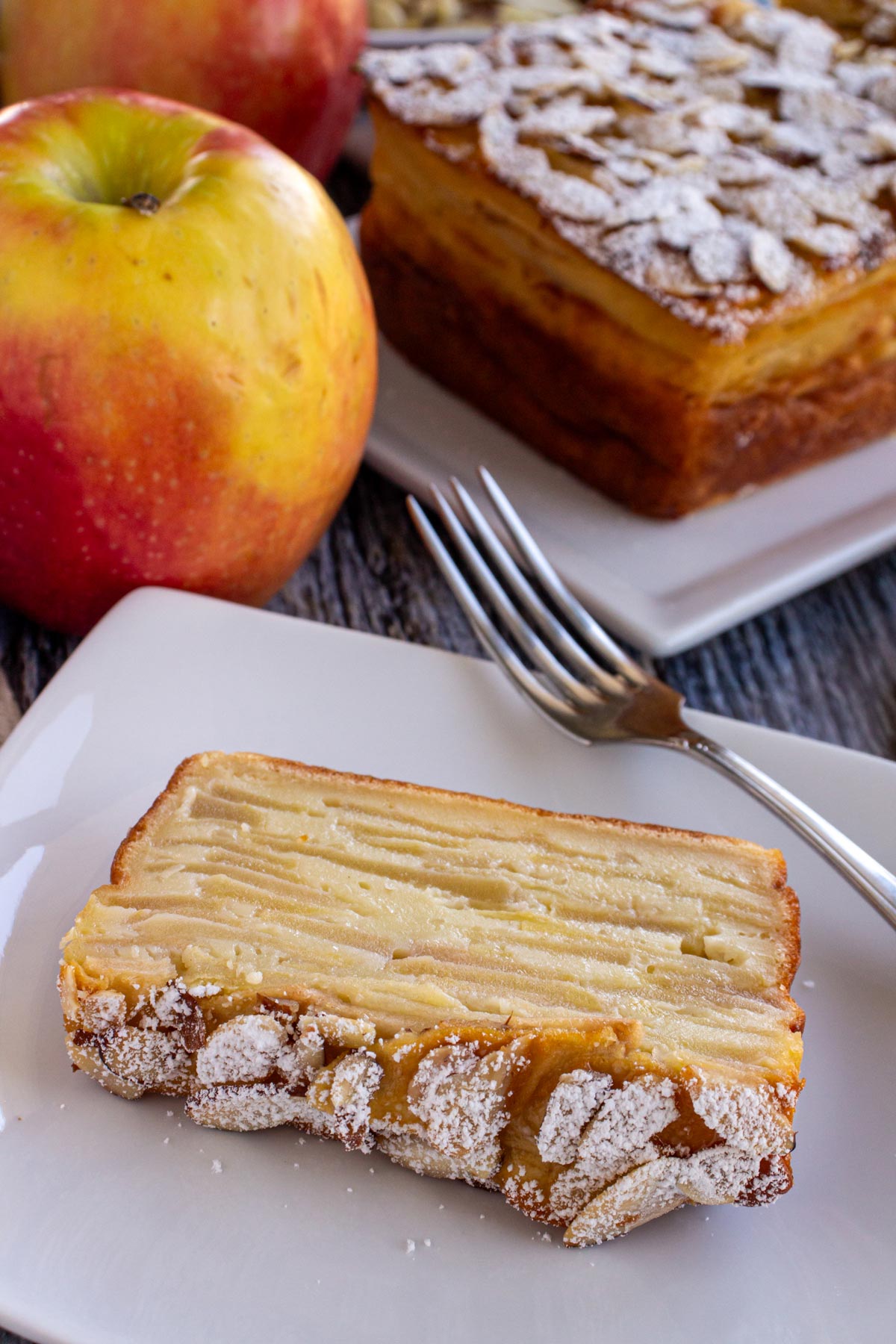 A slice of invisible apple cake topped with sliced almonds and powdered sugar.
