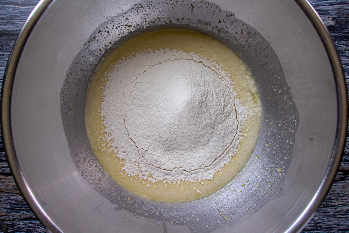 Flour sifted over the top of a liquid mixture in a metal mixing bowl.