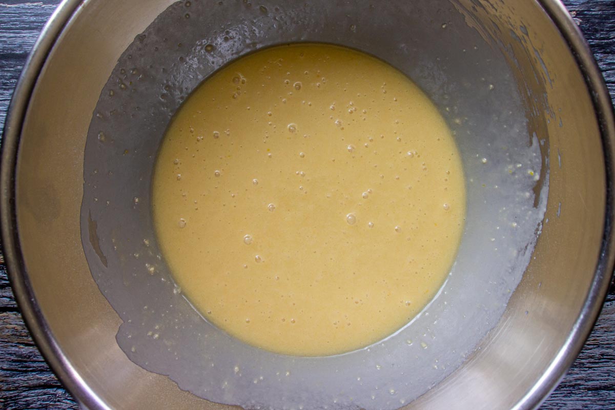 A thin custardy cake batter with several air bubbles in a metal mixing bowl.