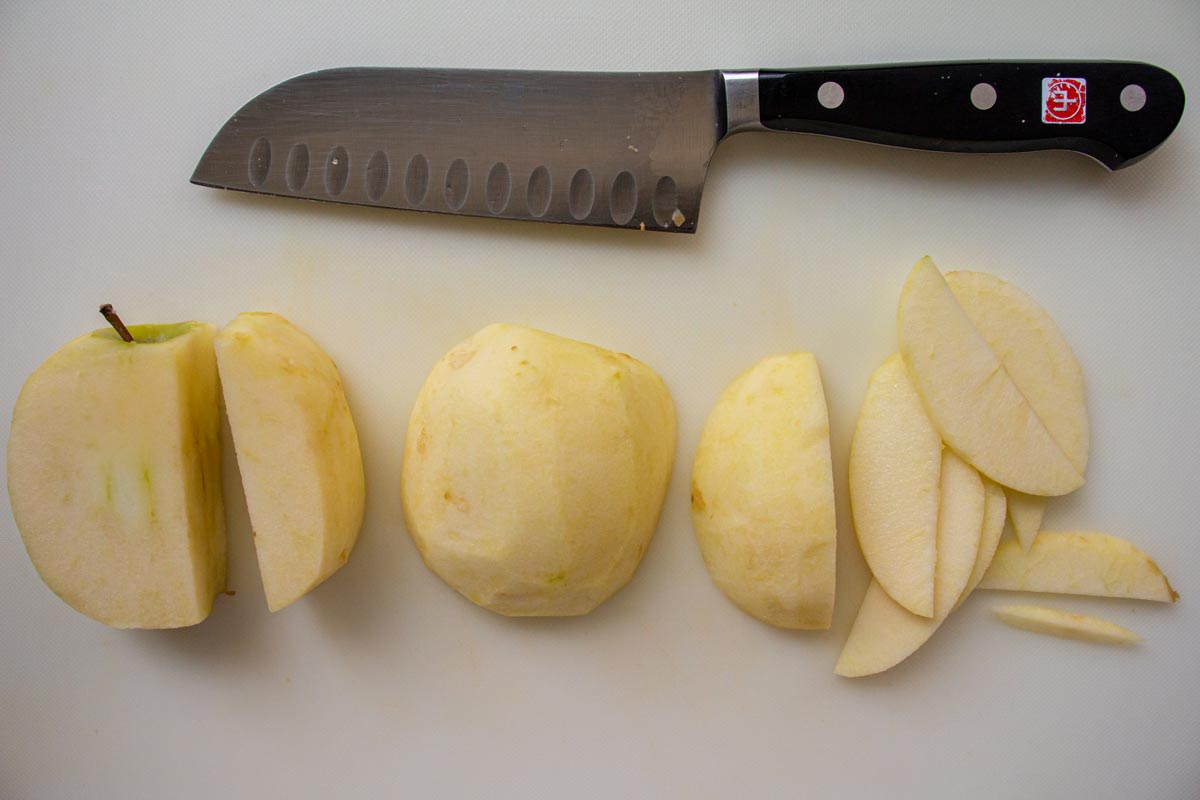 Slicing an apple into thin slices on a white cutting board with a knife.