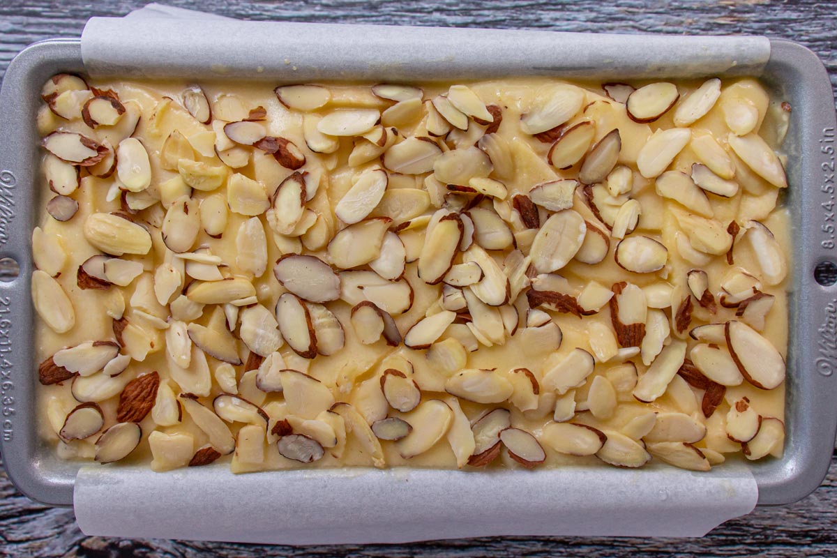 A mixture in a loaf pan topped with sliced almonds before baking.