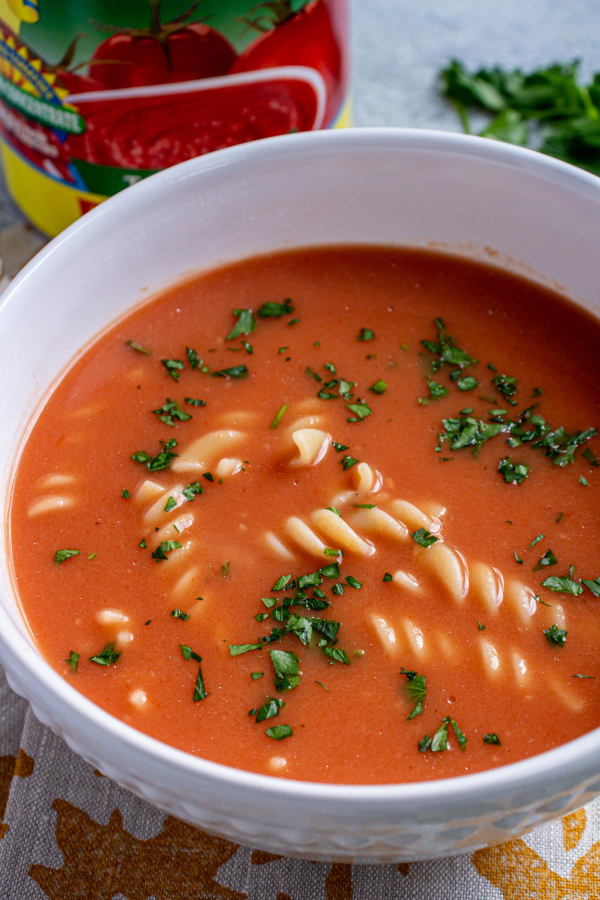 Closeup of a bowl of zupa pomidorowa with a can of tomatoes in the background.
