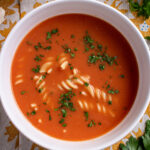 A bowl of zupa pomidorowa with rotini pasta, garnished with chopped parsley.