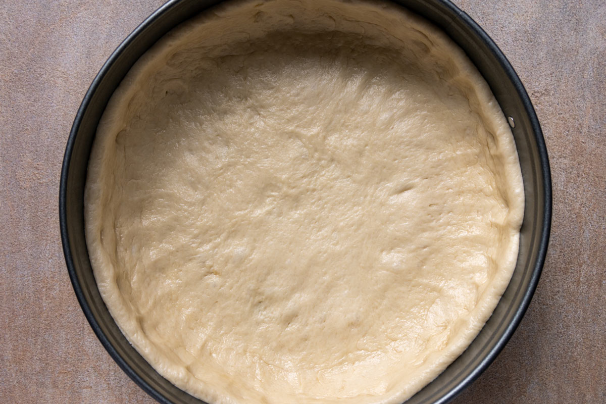 Yeast dough pressed into the bottom and sides of a springform pan.