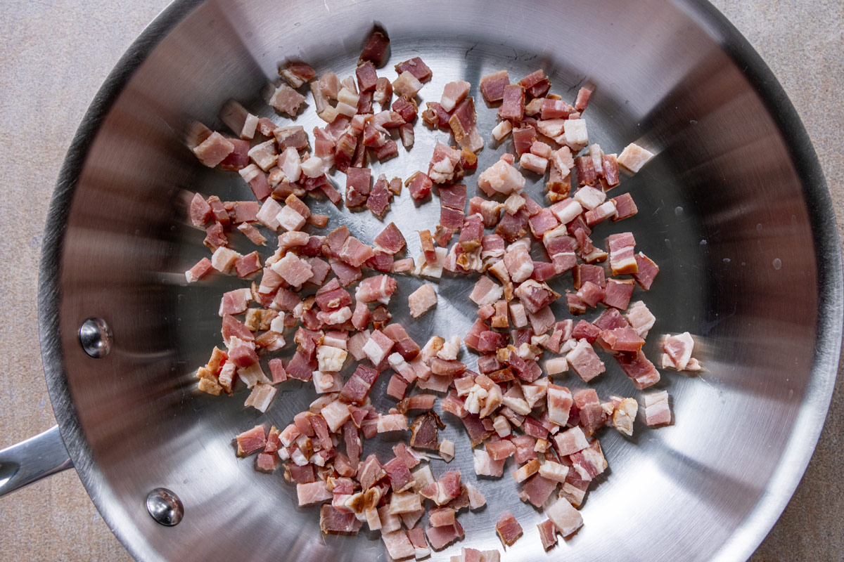 Diced thick-cut bacon in a stainless steel skillet before cooking.