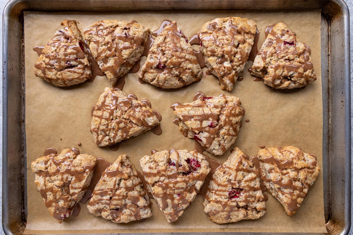 Baked cranberry apple scones on a sheet pan drizzled with cinnamon glaze.