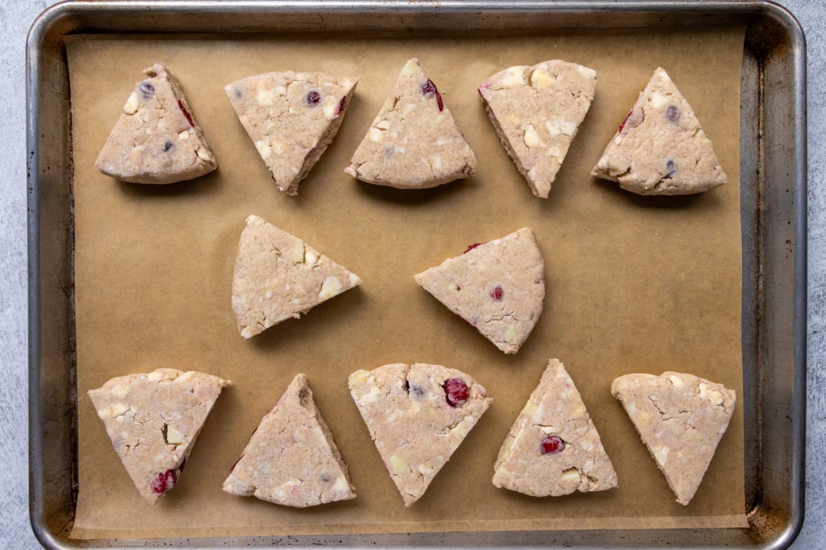 Unbaked triangular cranberry apple scones on a sheet pan.