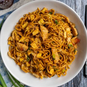 Mie goreng stir-fried noodles with chicken, diced omelet, and scallions in a white bowl.