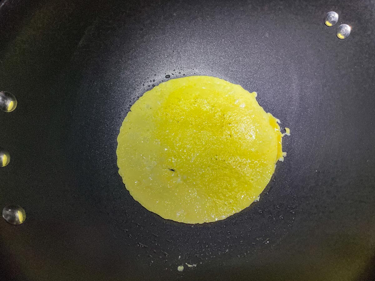 An omelet cooking in a wok after flipping it over.