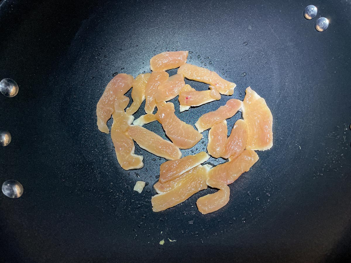 Thin strips of chicken cooking in a wok.
