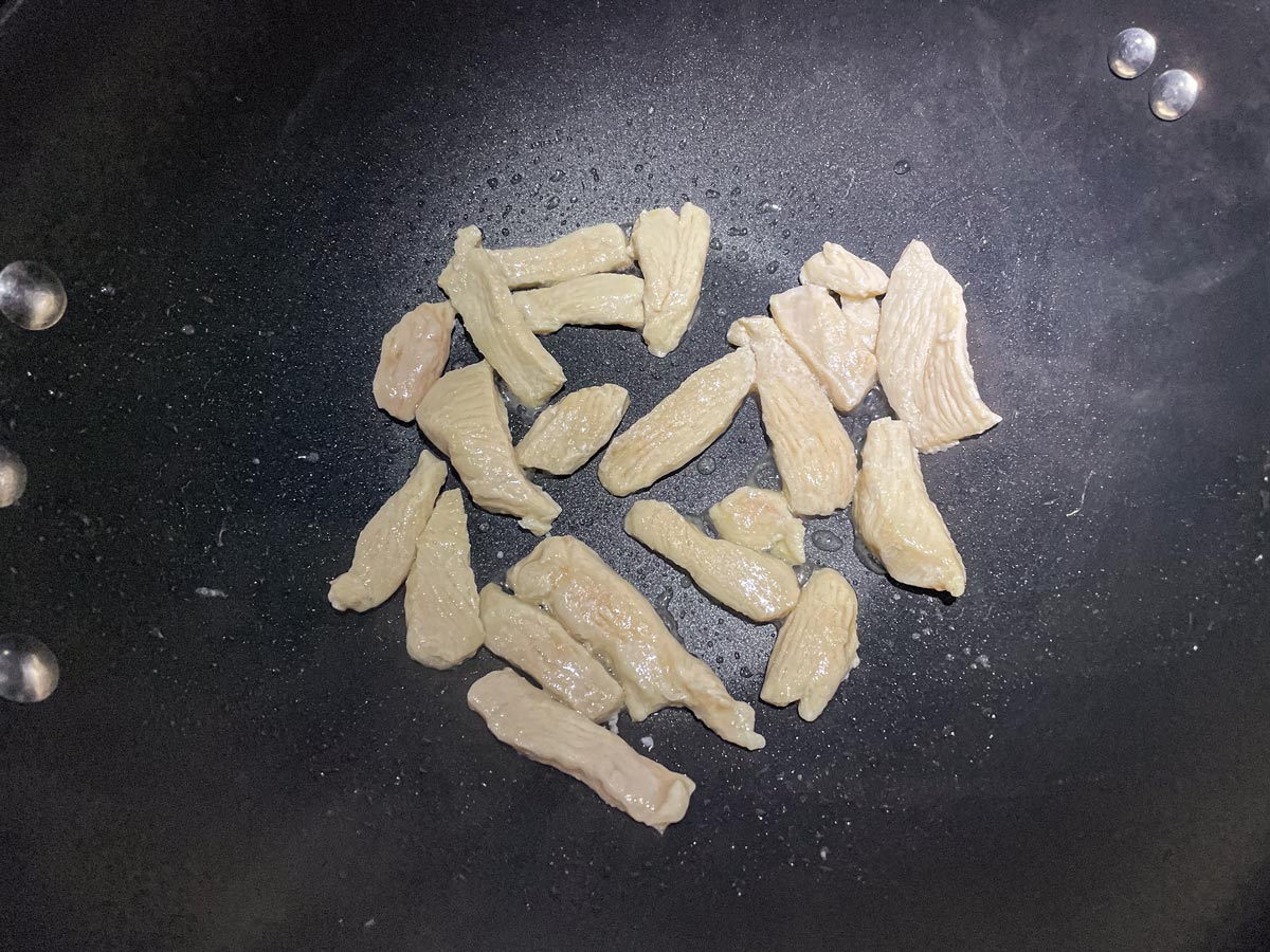 Thin slices of chicken cooking in a wok.