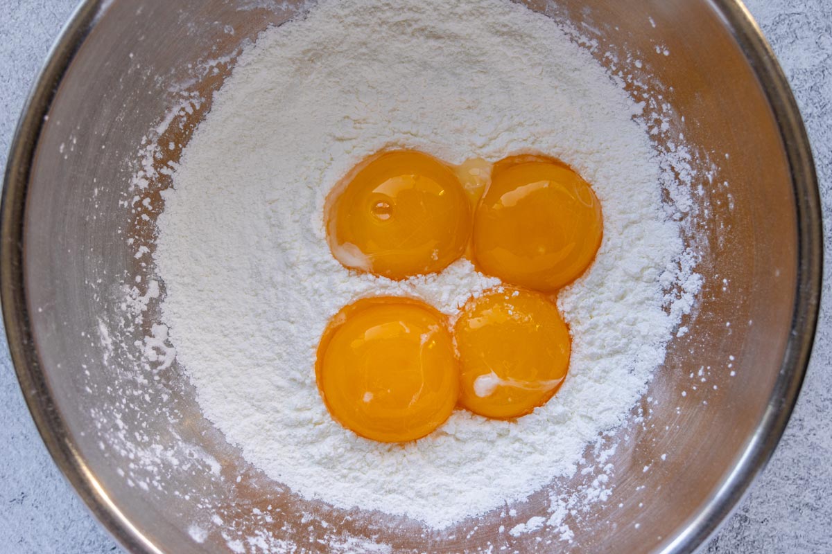 A metal mixing bowl with cornstarch, sugar, and 4 egg yolks on top.