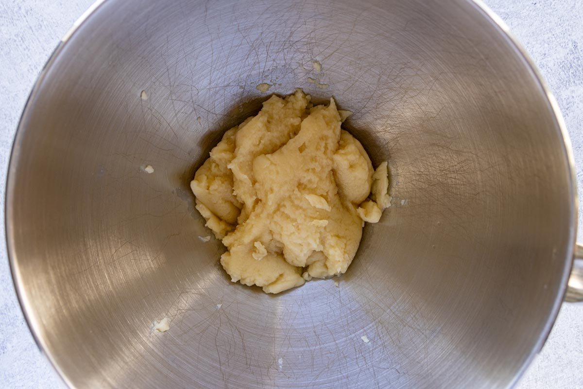 Dough for choux pastry cooling in a metal mixing bowl.