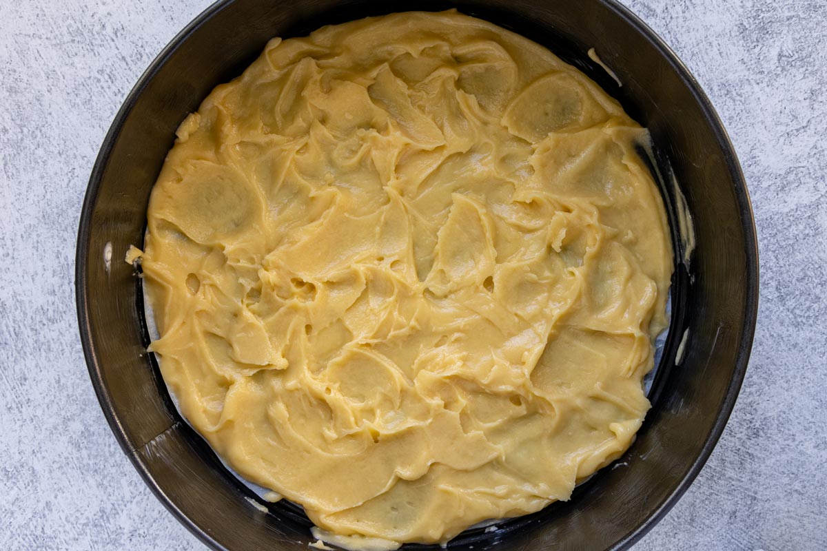 Choux dough spread out in an even layer with a rough surface in a springform pan.