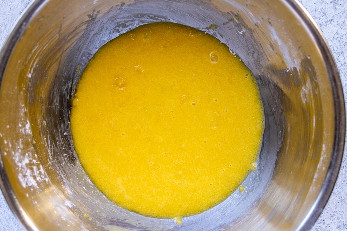A bright yellow mixture of egg yolks, cornstarch, and sugar in a metal mixing bowl.