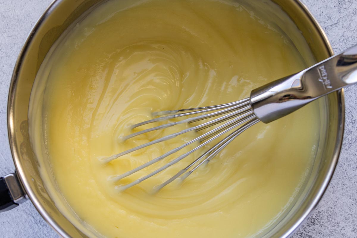 Thick pastry cream in a saucepan with a whisk inside.