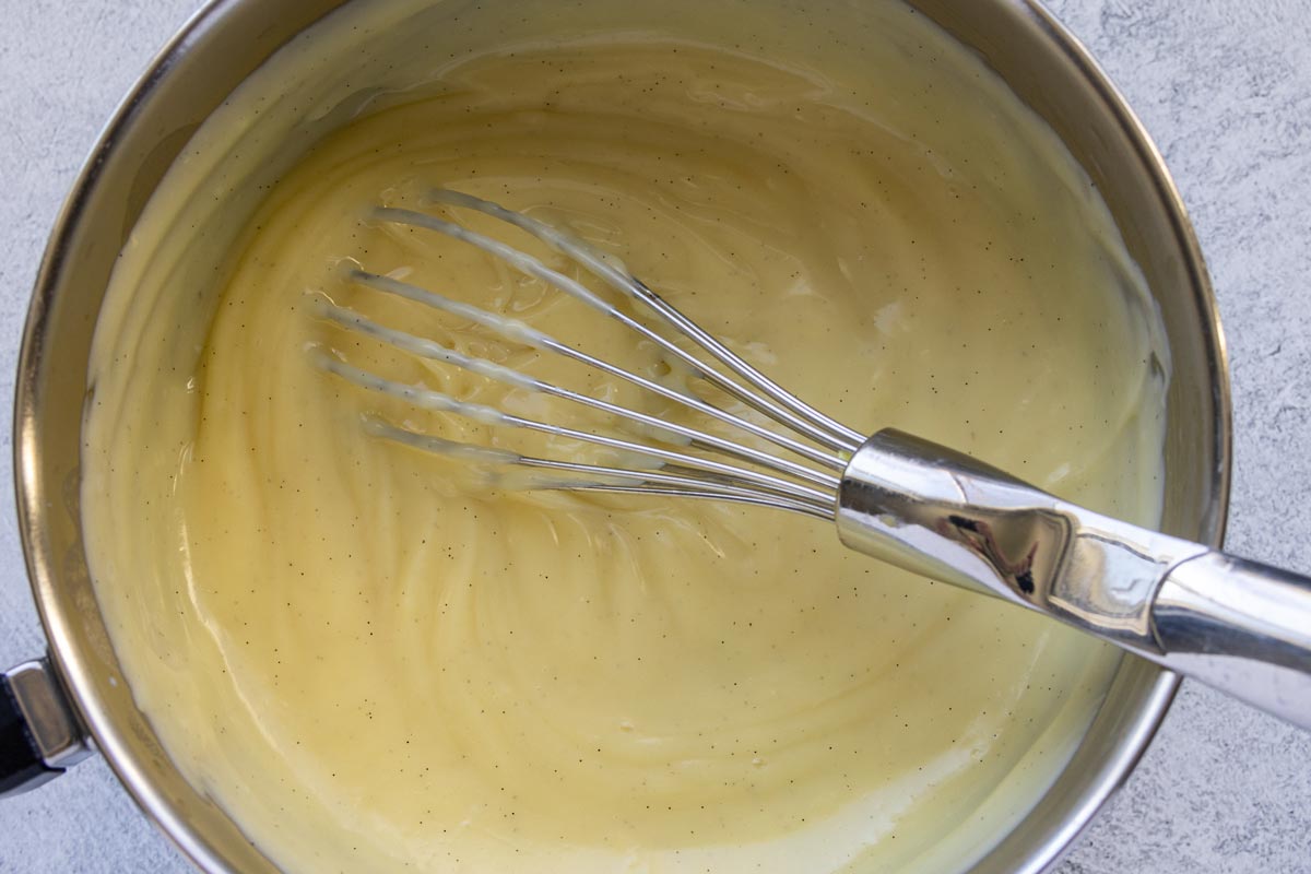 Thick pastry cream flecked with vanilla bean in a saucepan with a whisk.