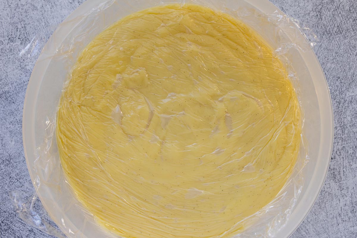 Pastry cream in a round plastic container with plastic wrap pressed to the surface.