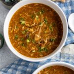 A bowl of Chinese hot and sour soup with shiitake mushrooms and tofu garnished with scallions.