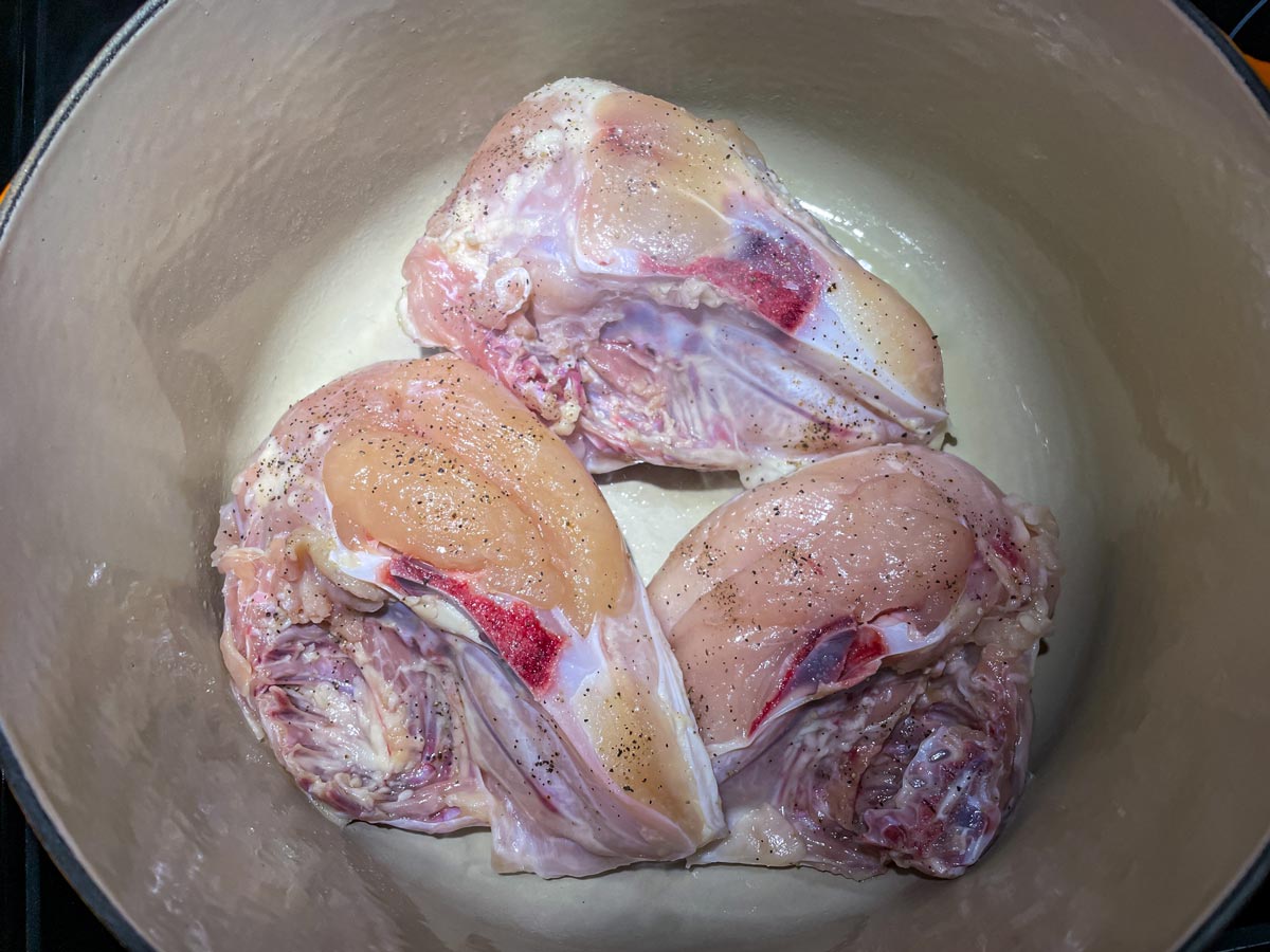 Three bone-in chicken breasts searing skin side-down in a Dutch oven.