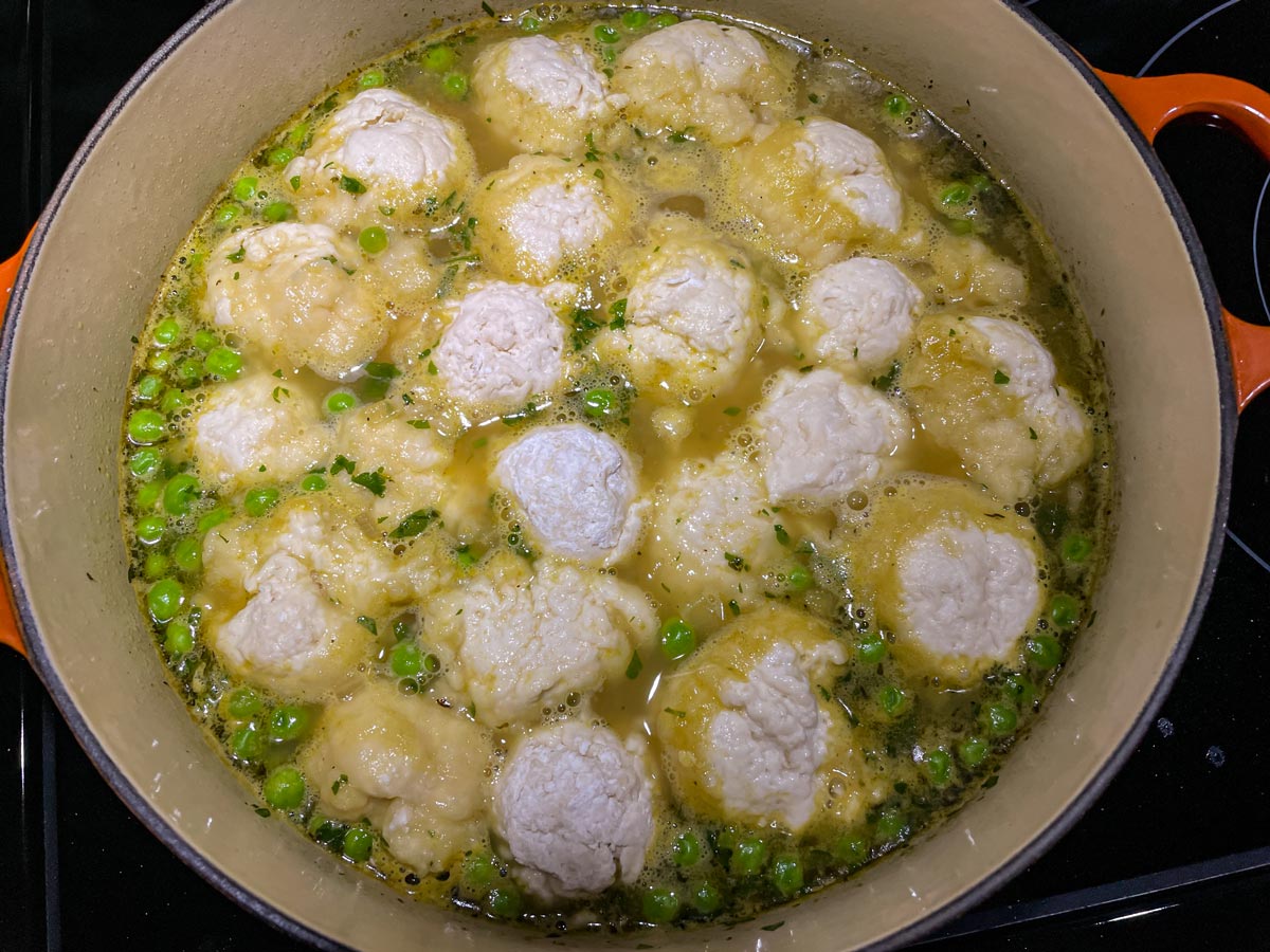 Scoops of dough floating on top of chicken soup with peas in a Dutch oven.