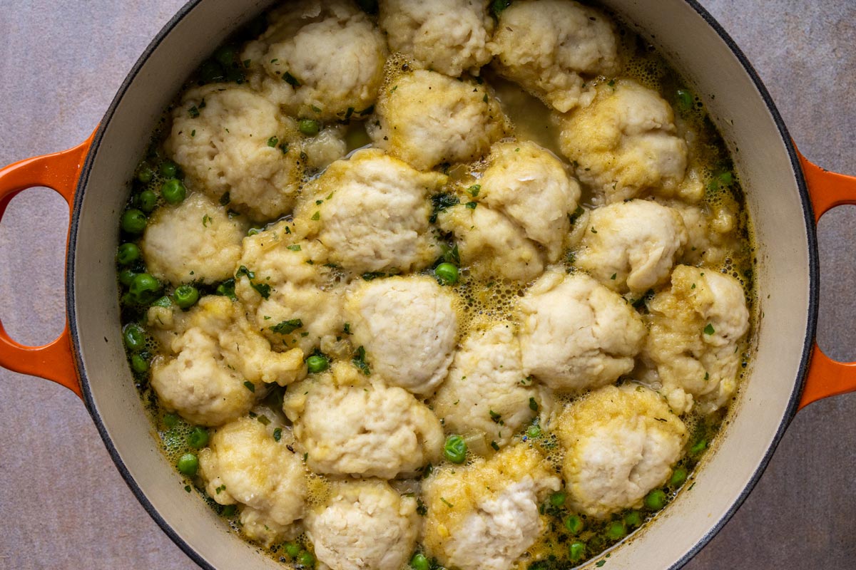 Steamed buttermilk dumplings floating on top of chicken soup with peas in a Dutch oven.