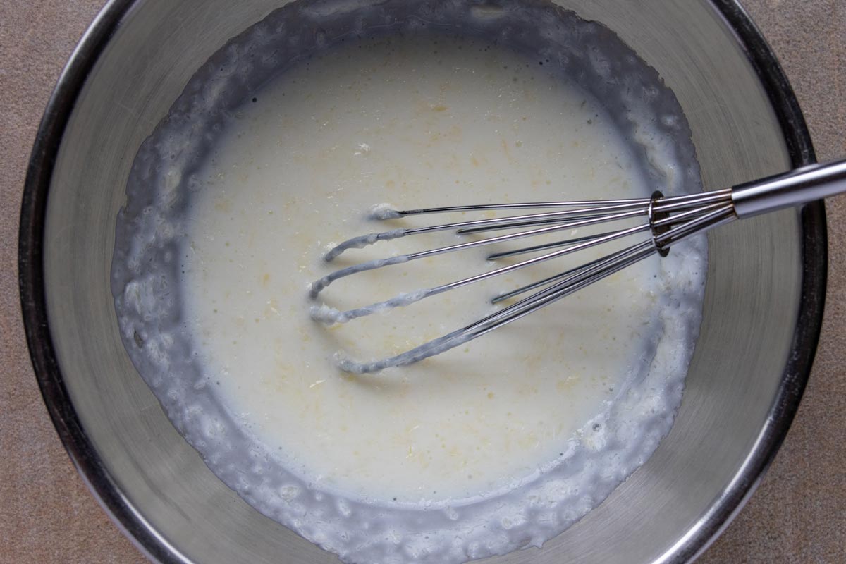 A mixture of buttermilk and melted butter in a metal bowl with a small whisk.