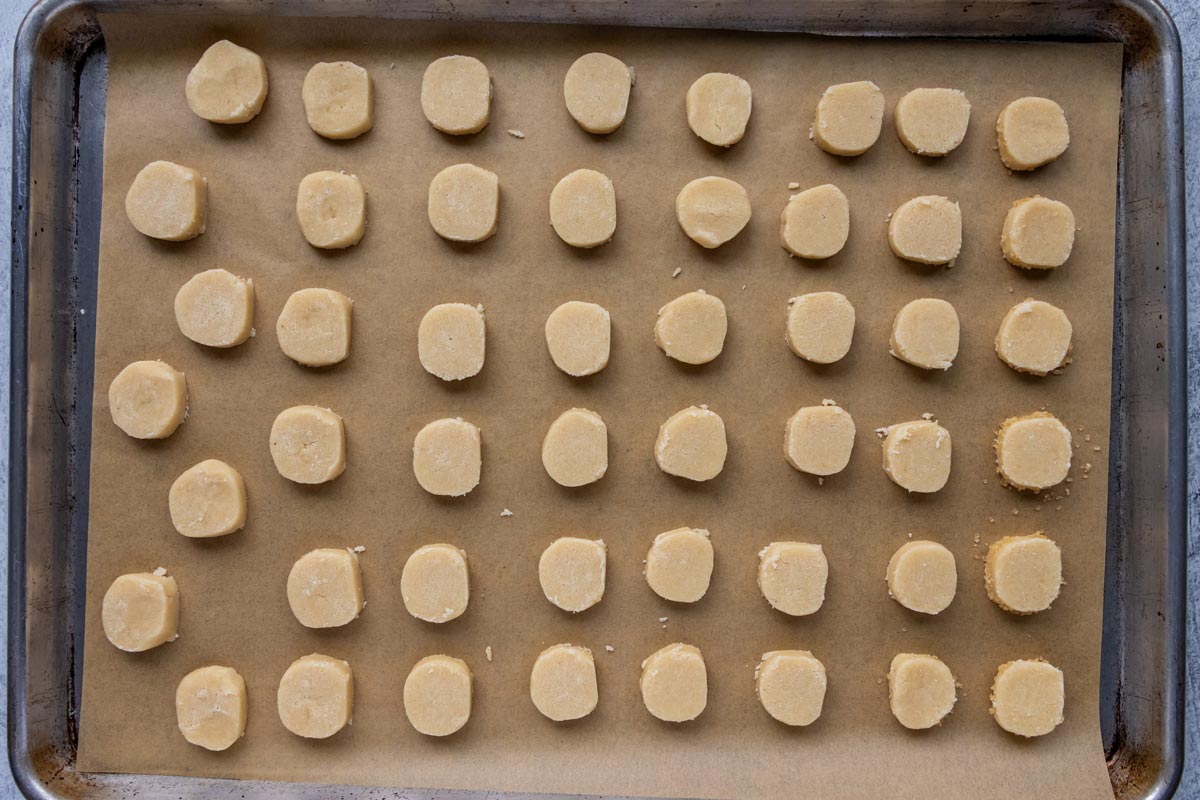 Sliced unbaked round shortbread cookies on a baking sheet.