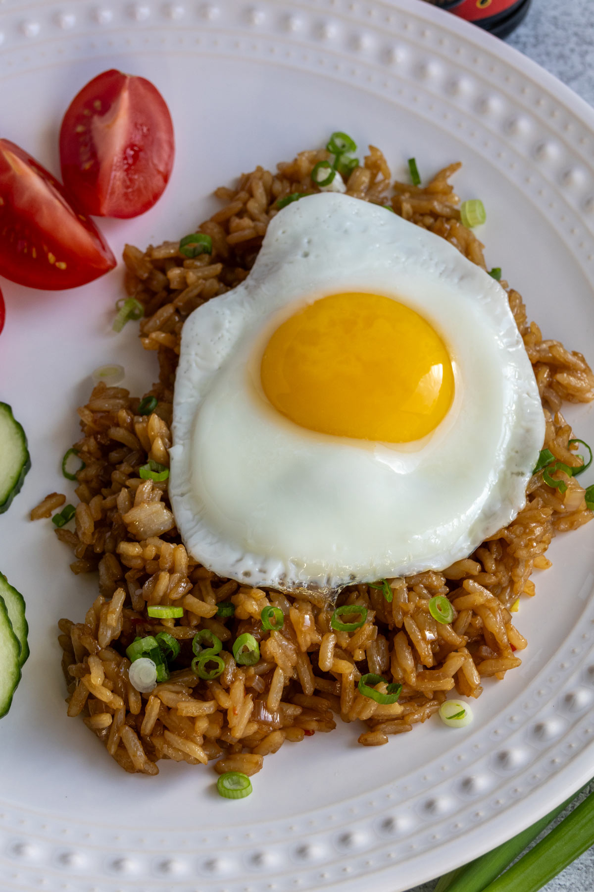 Fried rice topped with sliced scallions and a fried egg on a white plate.