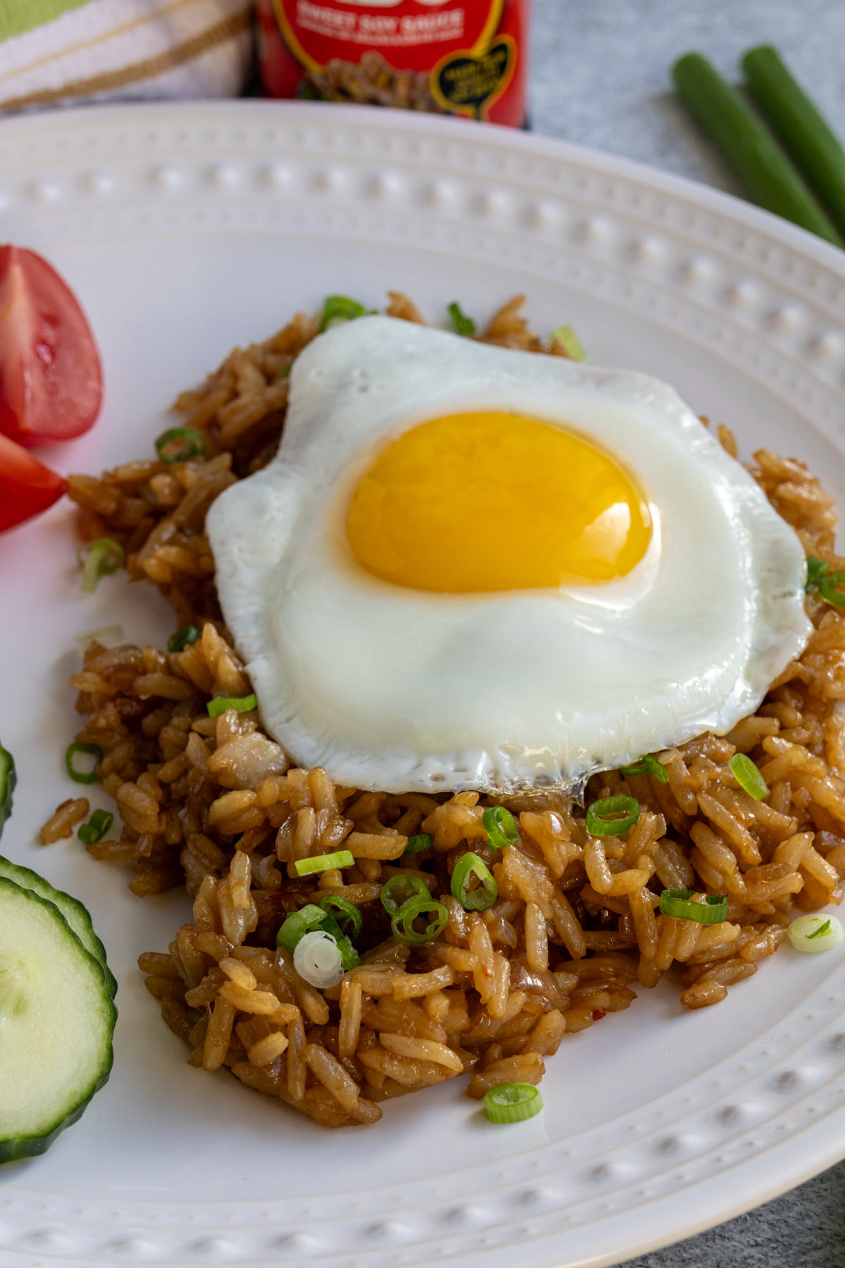 Indonesian fried rice topped with scallions and a fried egg on a white plate.