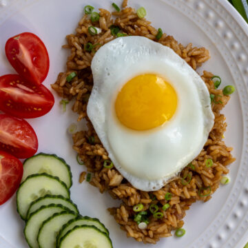 Nasi goreng topped with a fried egg with sliced cucumber and tomato on the side.