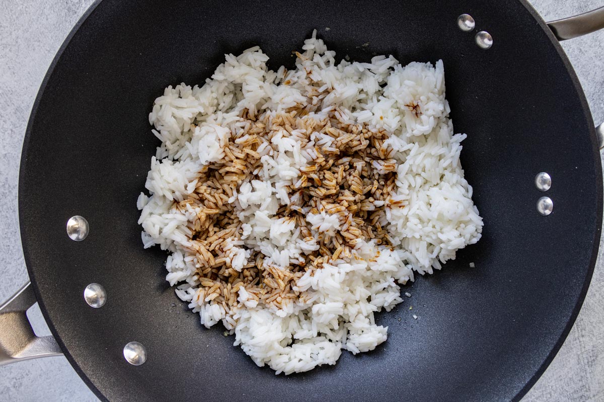 Cooked rice and soy sauce in a wok before tossing together.