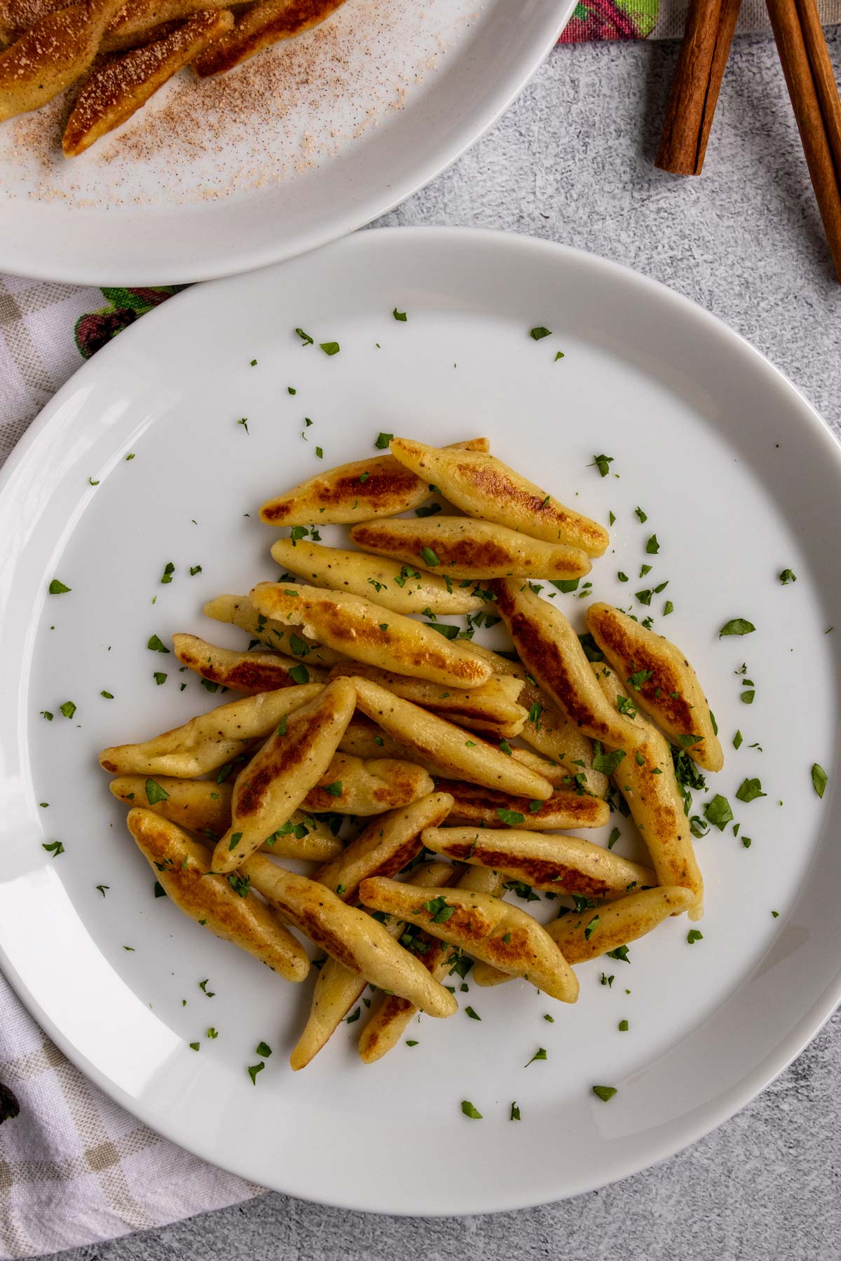 Pan-fried schupfnudeln potato noodles topped with chopped parsley on a white plate.