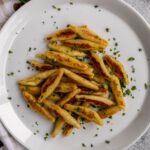 Pan-fried schupfnudeln potato noodles topped with chopped parsley on a white plate.
