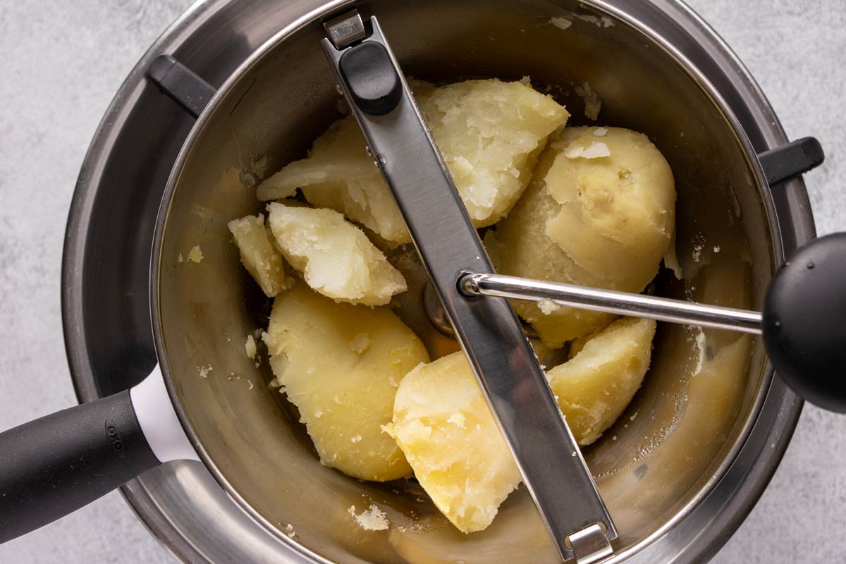 Large chunks of boiled potato in a food mill set over a metal bowl.