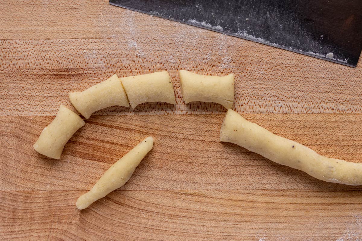 A rope of dough with pieces cut off and one shaped into a finger-shaped dumpling.