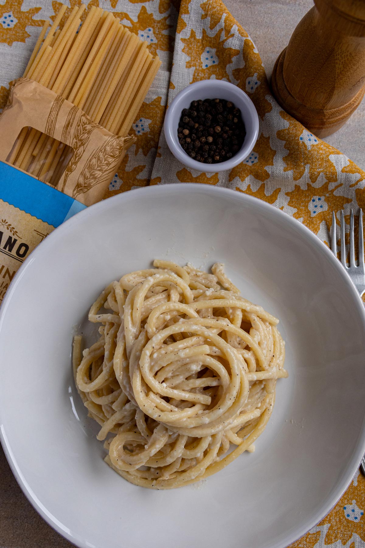 Bucatini cacio e pepe twirled into a pile in a wide white pasta bowl.