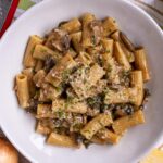 French onion soup pasta topped with grated cheese and chopped chives in a wide white bowl.