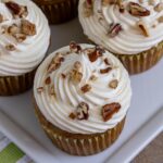 Hummingbird cupcakes with cream cheese frosting and chopped pecans arranged on a white platter.