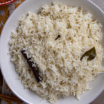Indian jeera rice with a cinnamon stick and bay leaf in a white serving dish.