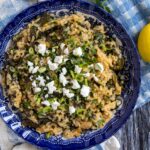 Greek spinach rice topped with crumbled feta in a blue and white shallow bowl.