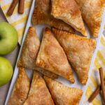 Golden brown triangular Dutch apple turnovers on a white rectangular platter.